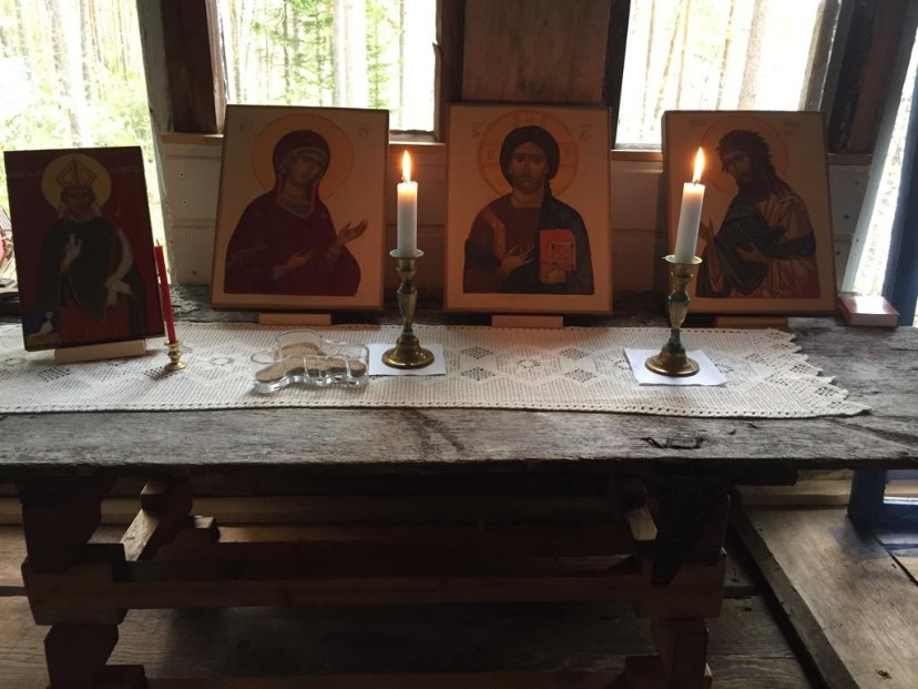 Harmaantuneella puupöydällä on neljä ikonia ja kynttilöitä.